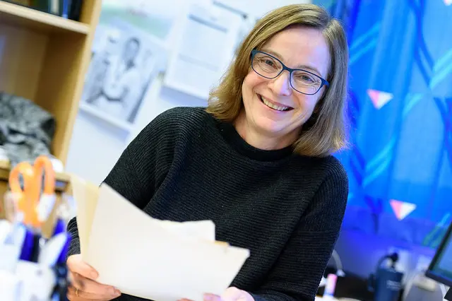 En smilende kvinne holder i en bunke med papirer.