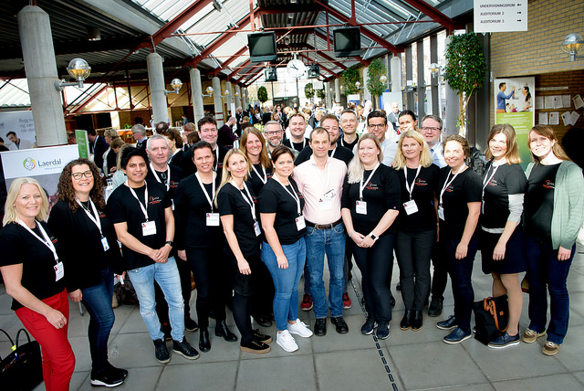 22 kvinner og menn står på to rekker og smiler inn i kamera.