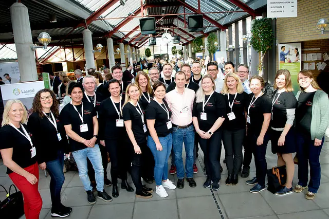 22 kvinner og menn står på to rekker og smiler inn i kamera.