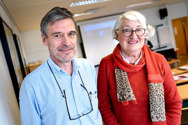 En mann i blått og en kvinne i rødt ser inn i kamera og smiler.