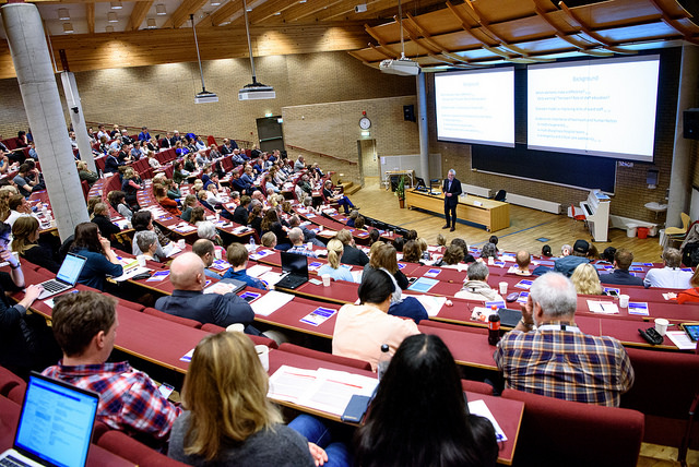 En stor forsamling av mennesker sitter og hører på en mannlig foredragsholder.