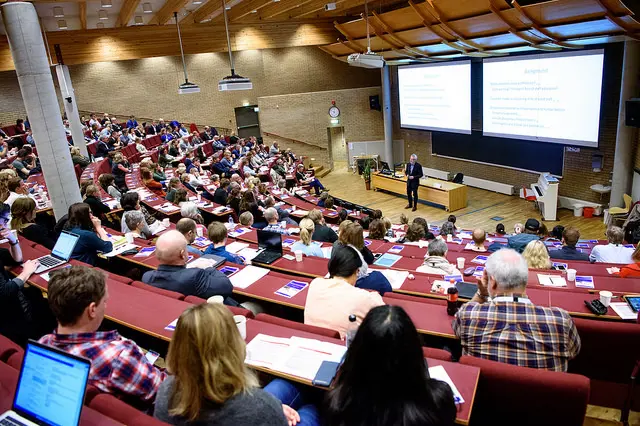 En stor forsamling av mennesker sitter og hører på en mannlig foredragsholder.