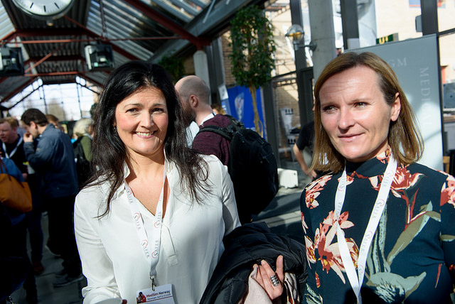 To kvinner. Den ene ser inn i kameraet og smiler, den andre ser litt bort til venstre.