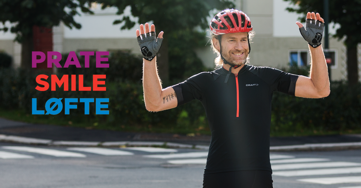 En smilende mann med skjegg og sykkelhjelm holder begge armene opp i været.