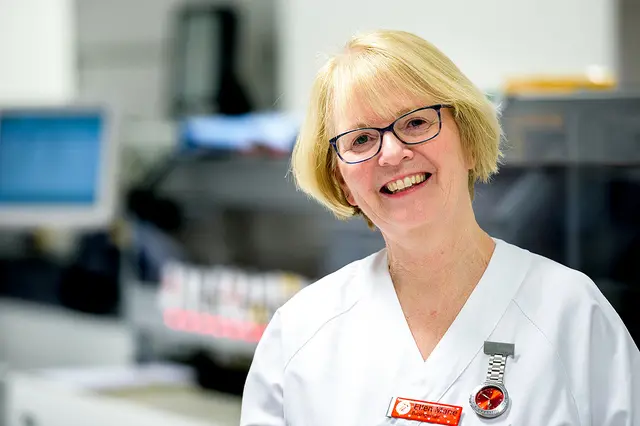 En lyshåret kvinne i hvite klær ser inn i kamera og smiler bredt.