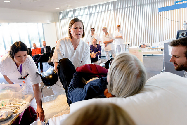 En liggende kvinne simulerer en fødsel og får hjelp av to jordmødre.