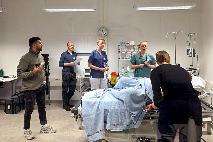 En gruppe mennesker står rundt en seng og simulerer