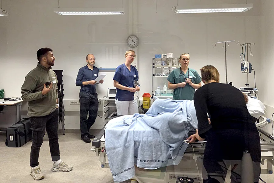 En gruppe mennesker står rundt en seng og simulerer