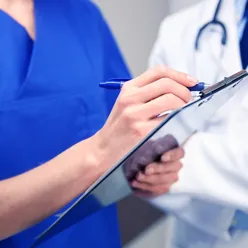 Bilde av kvinne som skriver på ark, mens mann observerer bak