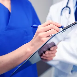 Bilde av kvinne som skriver på ark, mens mann observerer bak